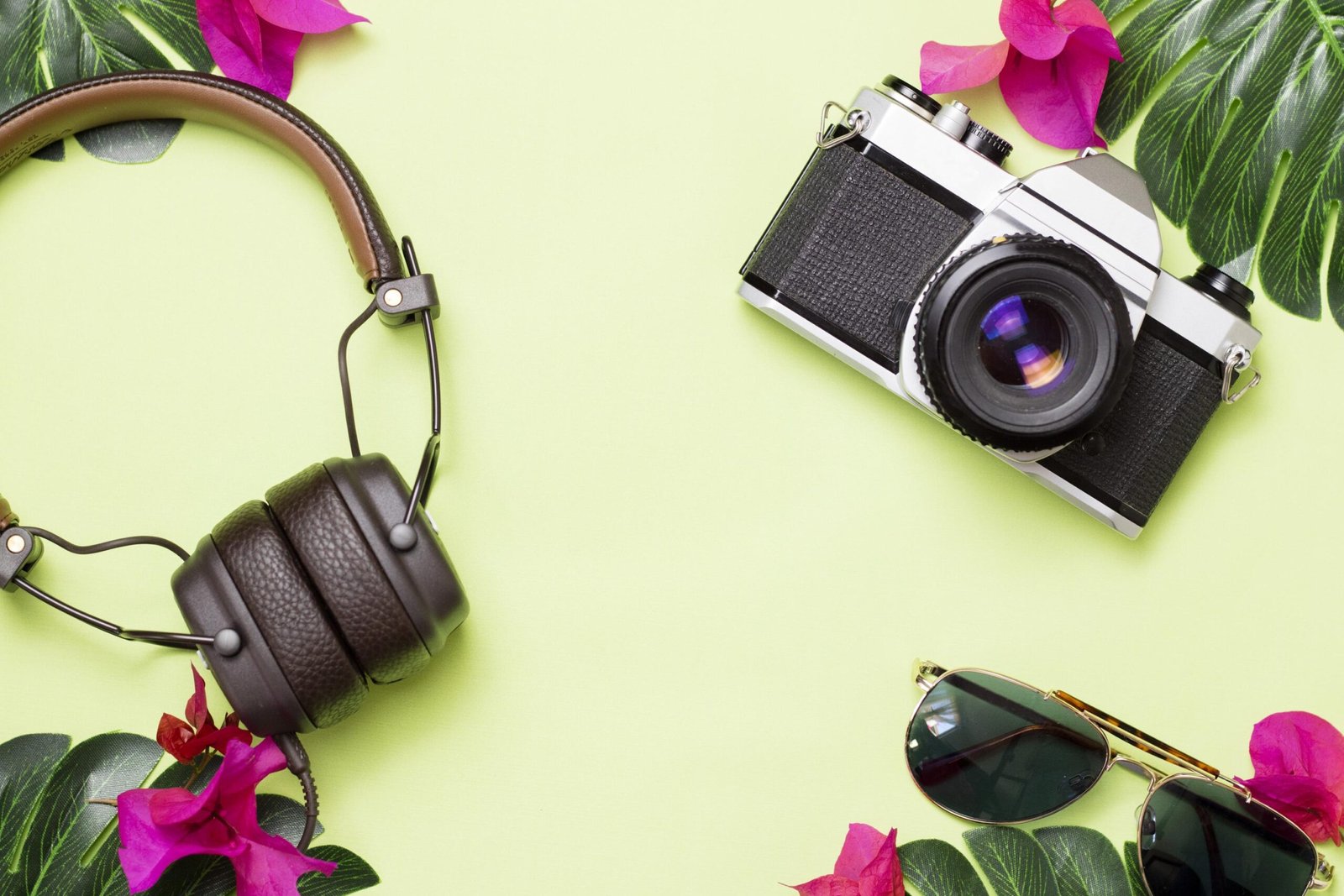 green-surface-with-retro-camera-headphones-glasses-with-tropical-flowers